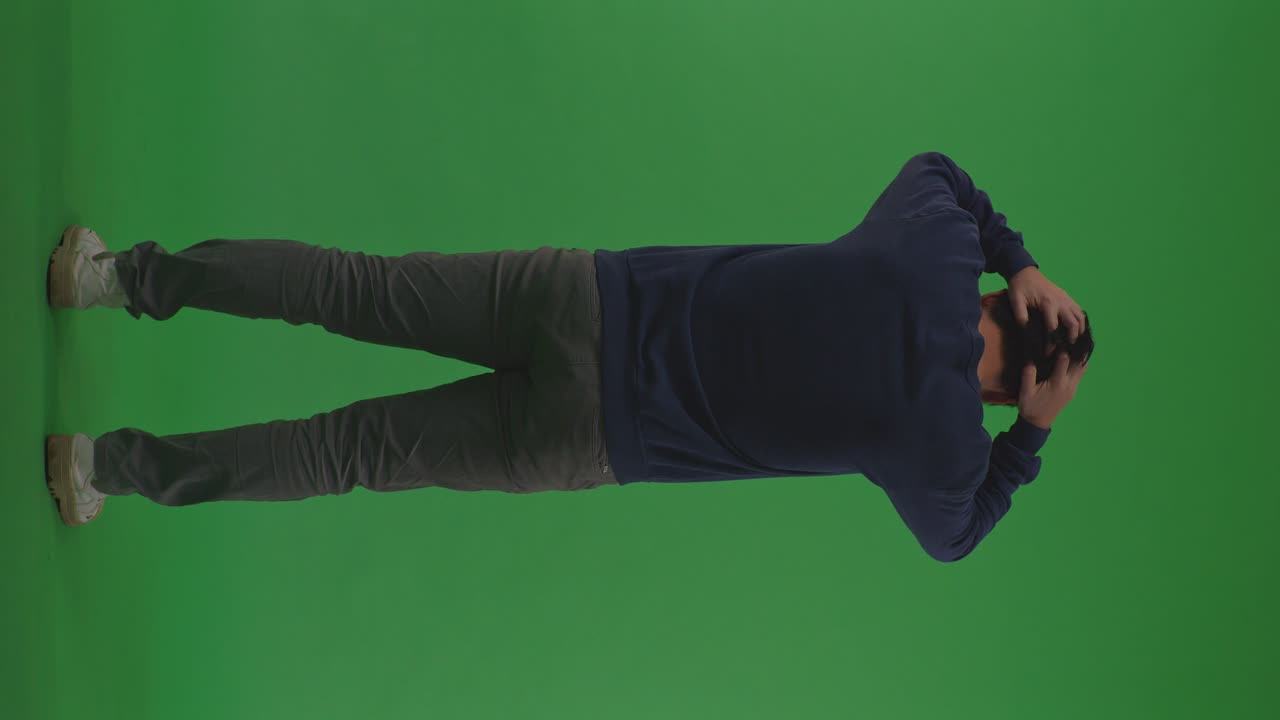 Full Body Back View Of Depressed Asian Refugee Male Rubs His Hands Through His Black Hair In Despair In The War While Standing On The Green Screen Background
