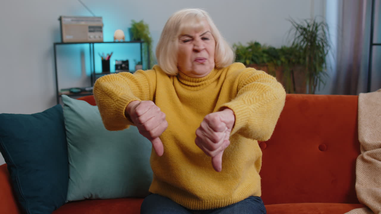 Upset grandmother woman showing thumbs down dislike bad work disapproval dissatisfied feedback home