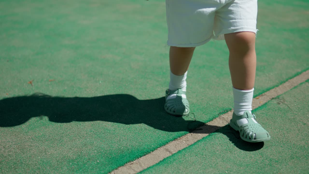 야외에서 녹색 배드민턴 코트를 걷고 있는 어린 소녀의 다리 - 슬로우 모션