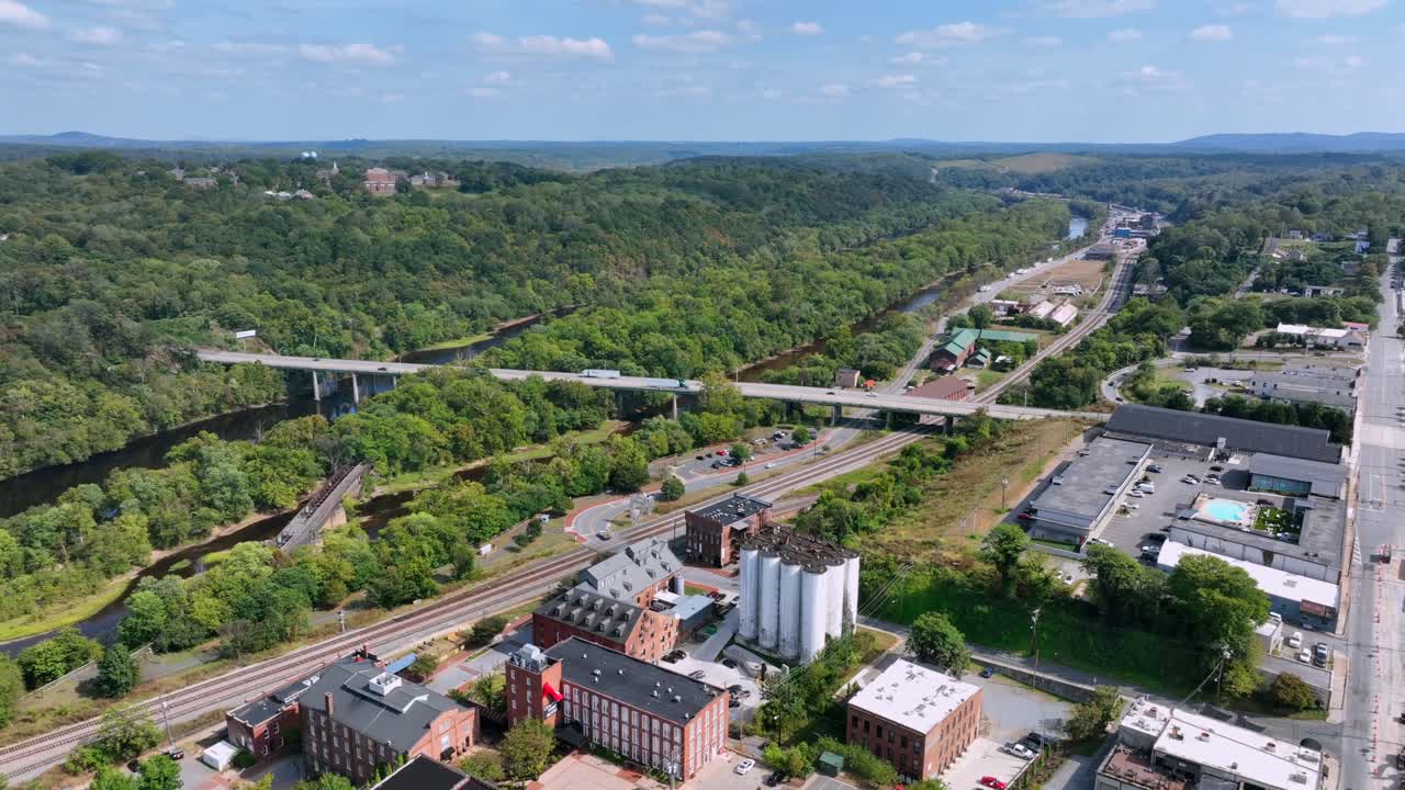 Aerial view of Lynchburg, Virginia, showing historic industrial buildings, river, bridges and surrounding green hills under clear sky. Late summer day in USA. Wide shot