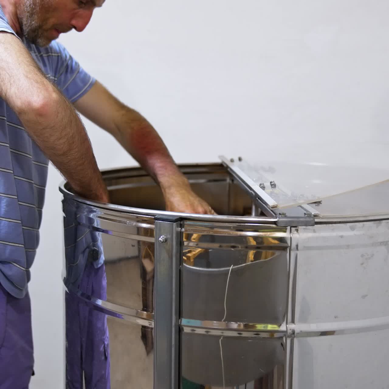 Apiarist preparing frames for honey extracting form cells. Male farmer places frames in a big metal barrel-like apparatus