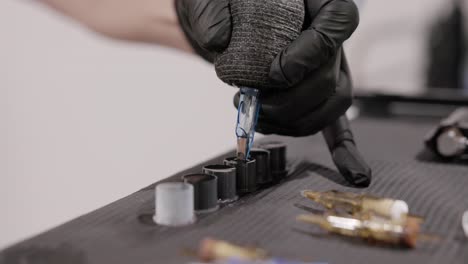 tattoo artist dips the tip of the needle cartridge into a filled ink cap on the table