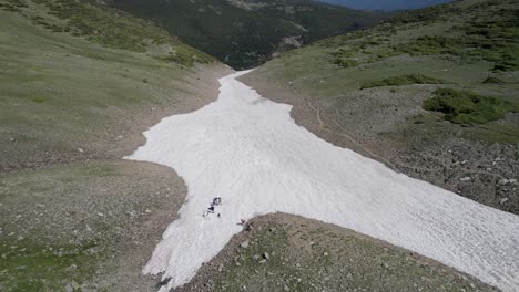 an orbiting 4k drone shot of a group of backcountry skiers preparing to ski down saint mary’s glacier, a semi-permanent snowfield located next to saint mary’s lake in colorado, usa