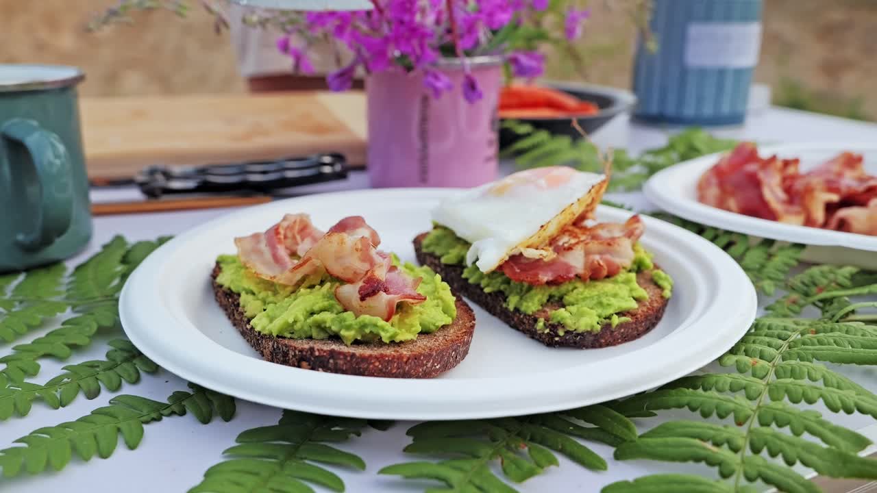 Golden fried egg placed in slow motion on crunchy toast with guacamole and bacon
