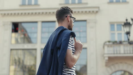 portrait of a handsome young man with a jacket over the shoulder posing and smiling at the camera in the street