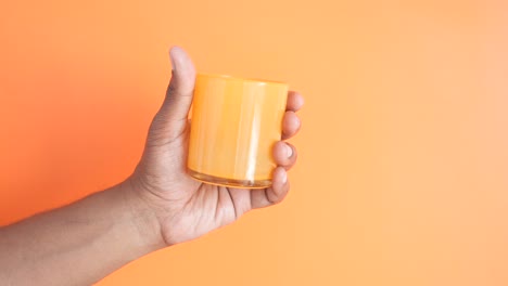 mano con una taza de vidrio naranja