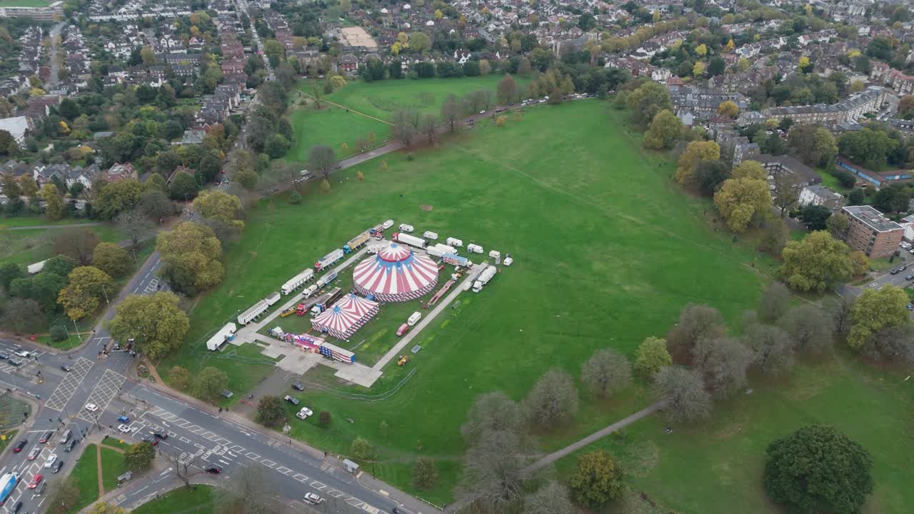 Aerial view of a vibrant circus tent set up on Ealing Common, surrounded by lush green fields and nearby residential areas, Ealing, London