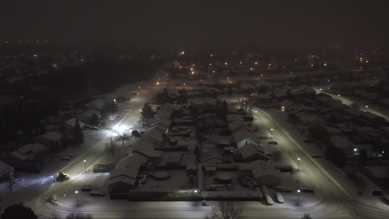 Aerial View Of Snow-covered Neighborhood At Night With Snowblower Tractor At Work. Saint-Constant, Quebec, Canada. sideways shot