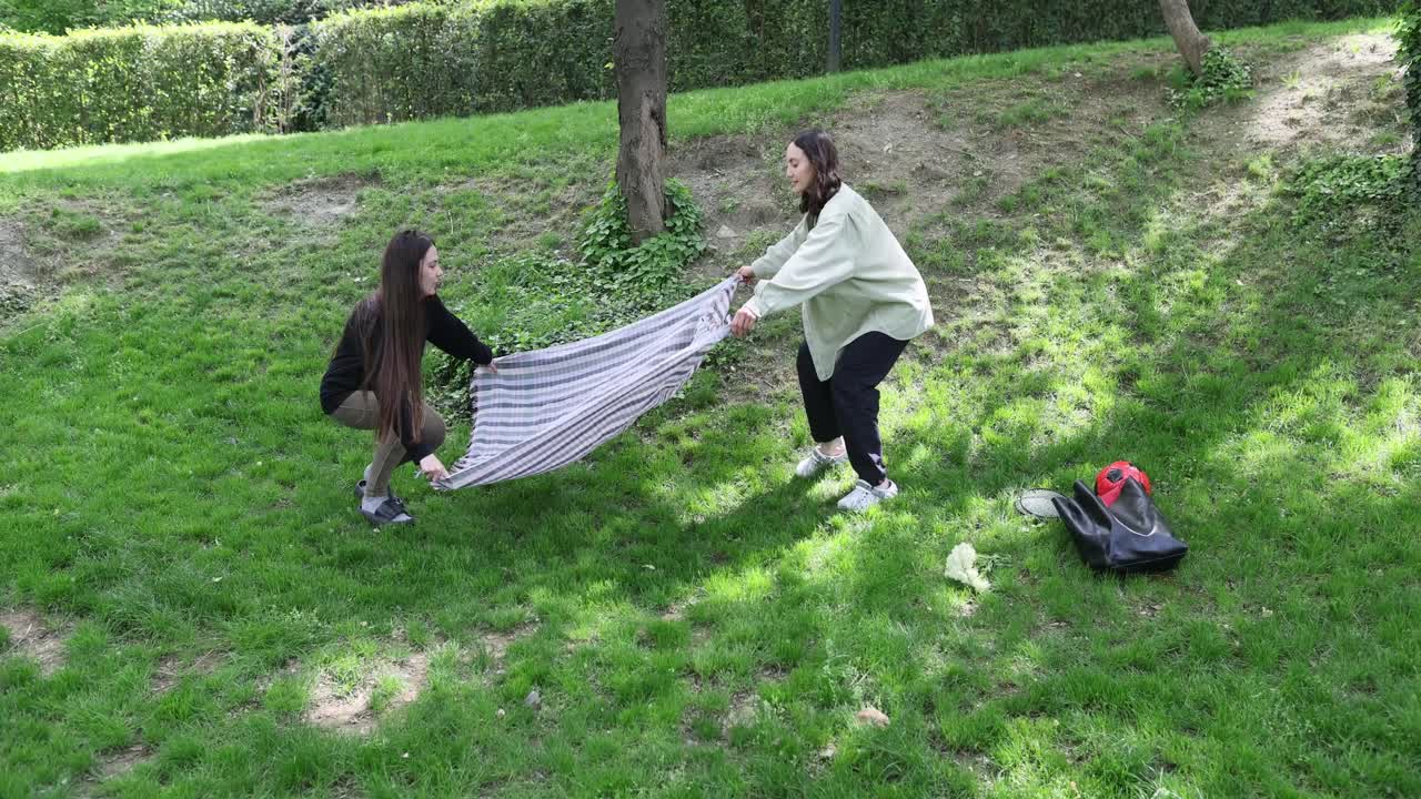 People laying a blanket on the grass in a park