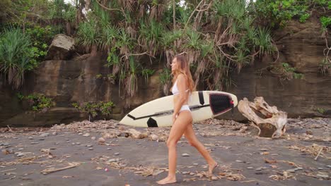 hermosa chica enfocada caminando en una playa de arena salvaje con su tabla de surf