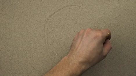 la mano masculina dibuja en la arena un rostro simbólico neutral de una persona. vista superior.