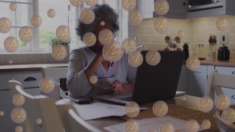 animation of coins over senior african american woman paying bills on laptop