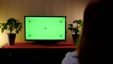 4k footage of woman sits on a couch in a living room, watches tv with a green screen