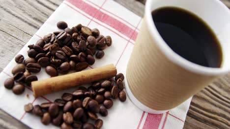 taza desechable con granos de café y canela en una tabla de madera