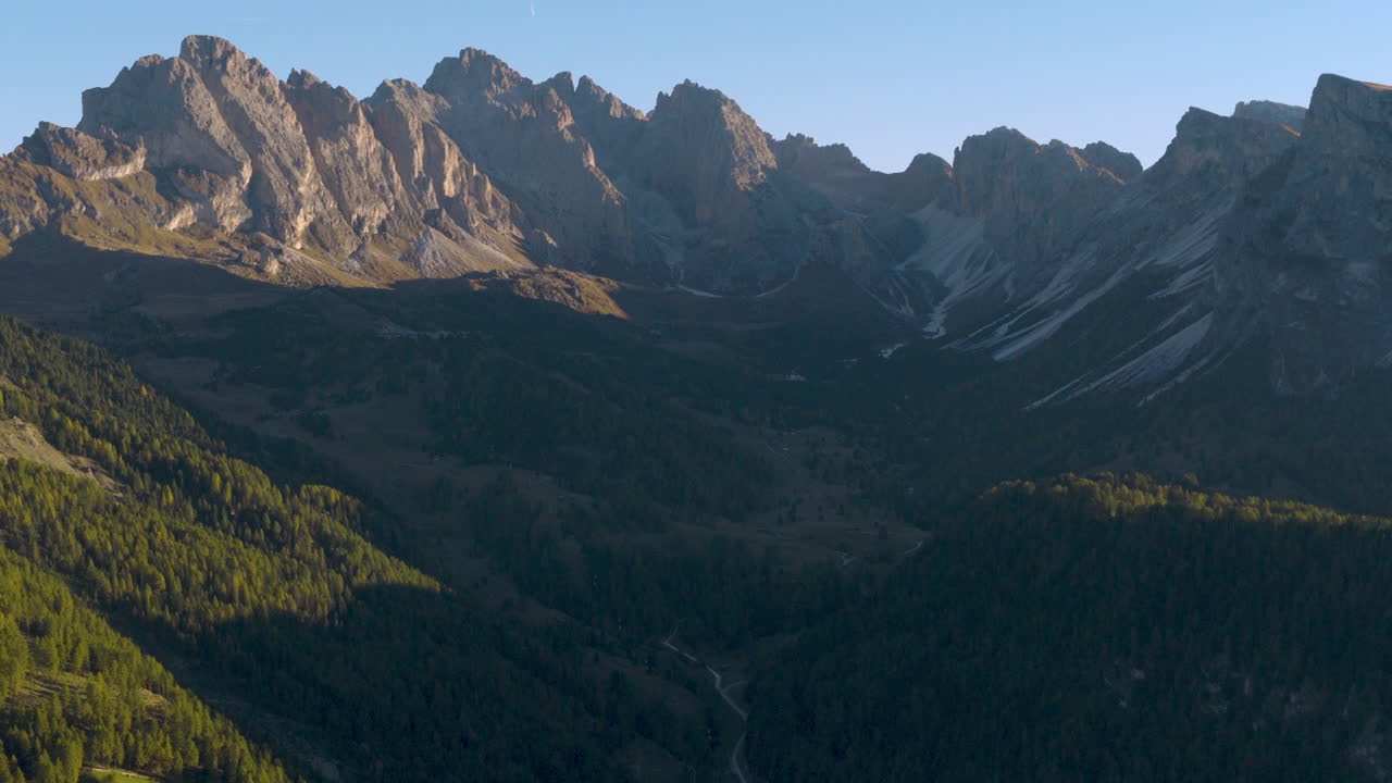 Pemandangan udara sinematik Dolomites di Italia, puncak alpine terjal yang bersinar saat fajar, tebing dramatis dan lembah berbayangan dalam menciptakan suasana ketinggian yang tenang