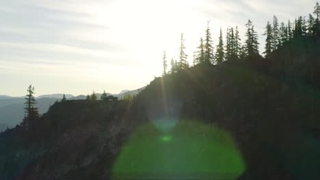 Aerial-of-silhouette-trees-on-top-of-mountain-ridge-with-one-pick-up-truck-parked-on-cliffs-edge,-bright-light-rays-from-sun,-sideways-motion