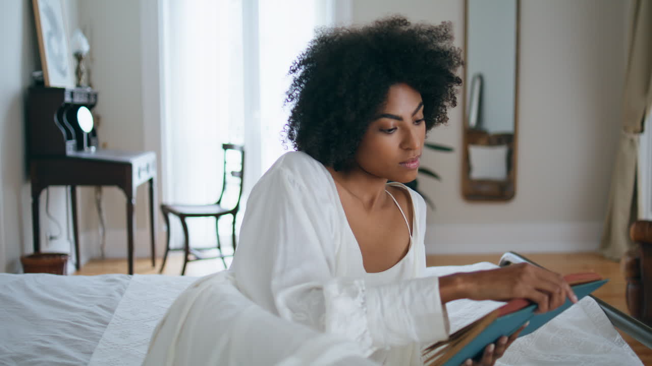 Peaceful girl read novel bed alone. African woman laying bedroom flipping pages