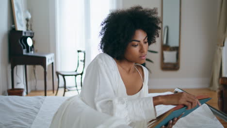 Peaceful-girl-read-novel-bed-alone.-African-woman-laying-bedroom-flipping-pages