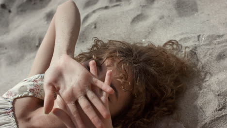 seductive lady lying beach sand hiding face behind hands closeup. woman smiling