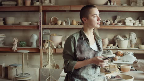 female potter using phone in workshop