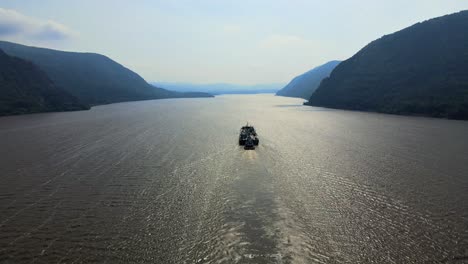 Aerial-drone-video-footage-of-a-large-cargo-ship-on-the-Hudson-River-in-New-York's-Hudson-Valley,-going-through-the-Hudson-Highlands-on-a-sunny-day-in-late-summer-or-early-fall