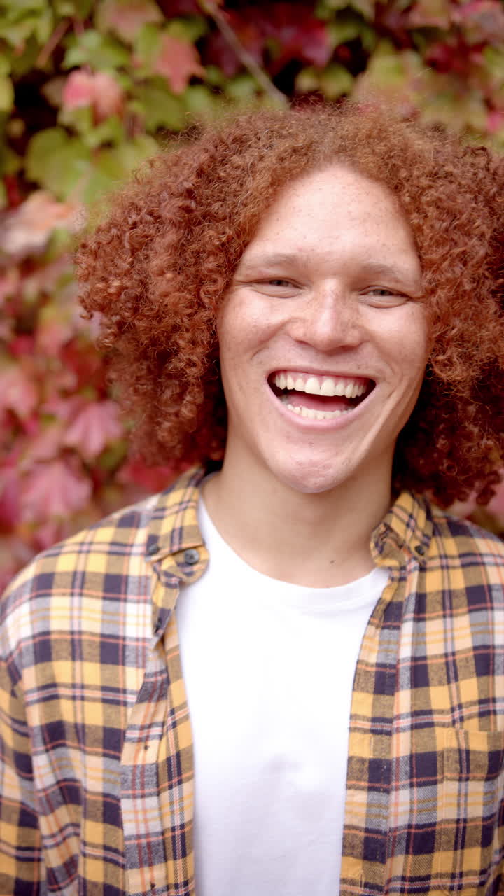 Vertical video of portrait of biracial man looking at camera and smiling, in slow motion