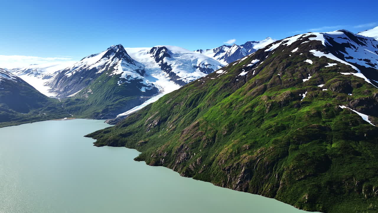 Glacial fjord and snowy Alaska peaks. Turquoise glacial water fills a steep fjord between rugged snowcapped Alaska mountains