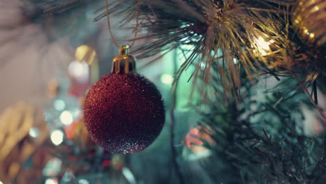 red glittery bauble dangling on christmas tree with glowing bokeh lights - closeup shot