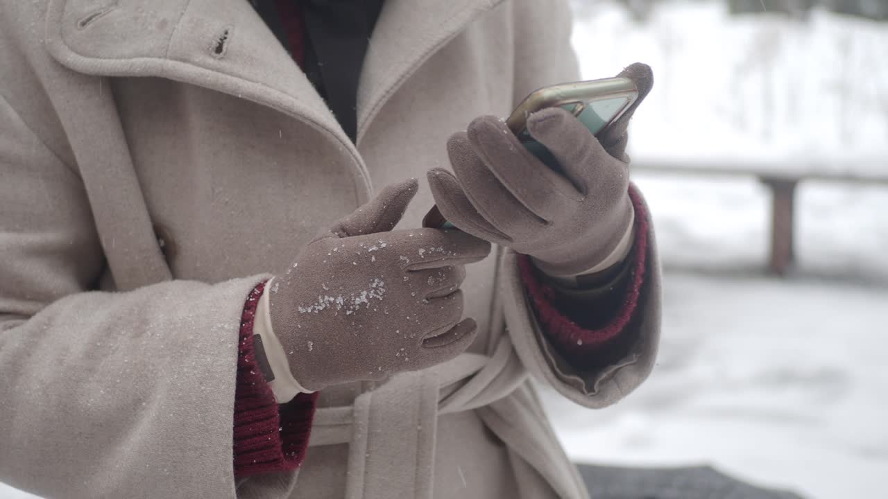 Hænder i handsker, der bruger smartphone i vintersne.
