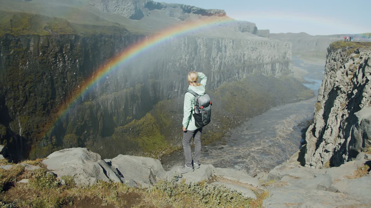 mujer de pie en el borde de un acantilado mirando hacia el cañón con el río de montaña cerca de la cascada de detifoss en islandia