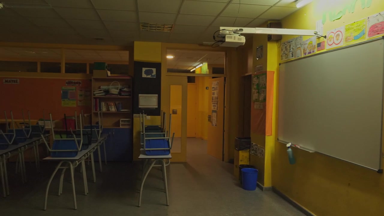 Mjuk bakåtgående kamerarörelse avslöjar ett mörkt och tomt skolklassrum på natten eller efter stängning. Bilden visar en interaktiv whiteboardtavla, overheadprojektor och anslagstavlor med elevkonstverk