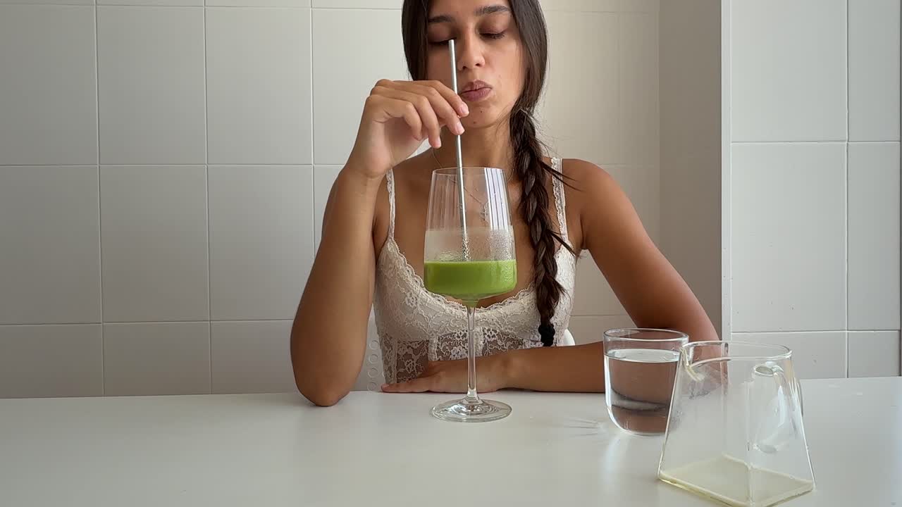 Giovane donna che mescola una bevanda verde e beve acqua