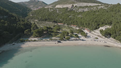 Disparo-De-Inclinación-De-Dron-De-5k-Desde-El-Mar-Azul,-La-Playa-Arenosa-De-Prapratno-Y-La-Ladera-Verde-En-Croacia-En-Un-Día-Soleado