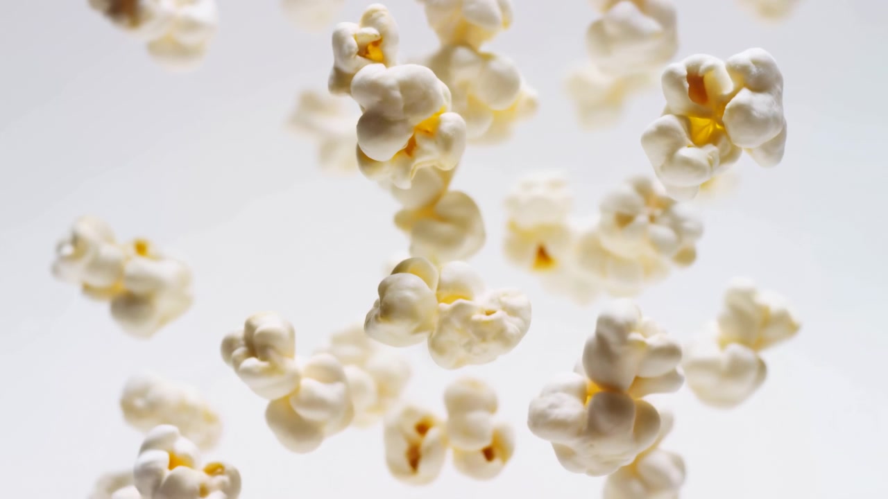 Närbild av poppade popcornkärnor på ren vit bakgrund, som visar fluffiga vita ytor, blekgula centra, oregelbundna veck, mjuka skuggor och krispig textur i en minimalistisk studiokomposition