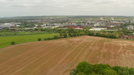 Disparo-Aéreo-Descendente-De-Tierras-De-Cultivo-Mirando-Hacia-Una-Pequeña-Ciudad-Industrial-Inglesa