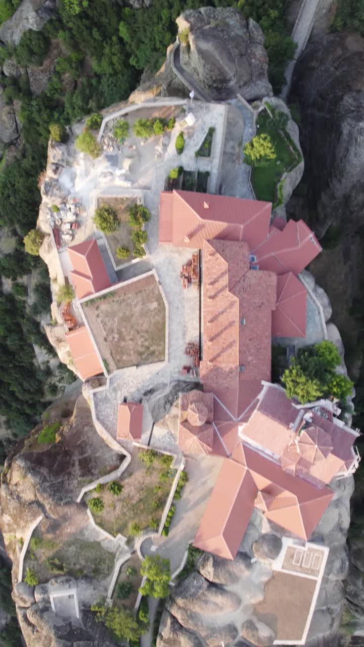 Vertical overhead aerial showcasing a monastery perched atop a rocky precipice, part of a UNESCO World Heritage site, surrounded by dramatic cliffs