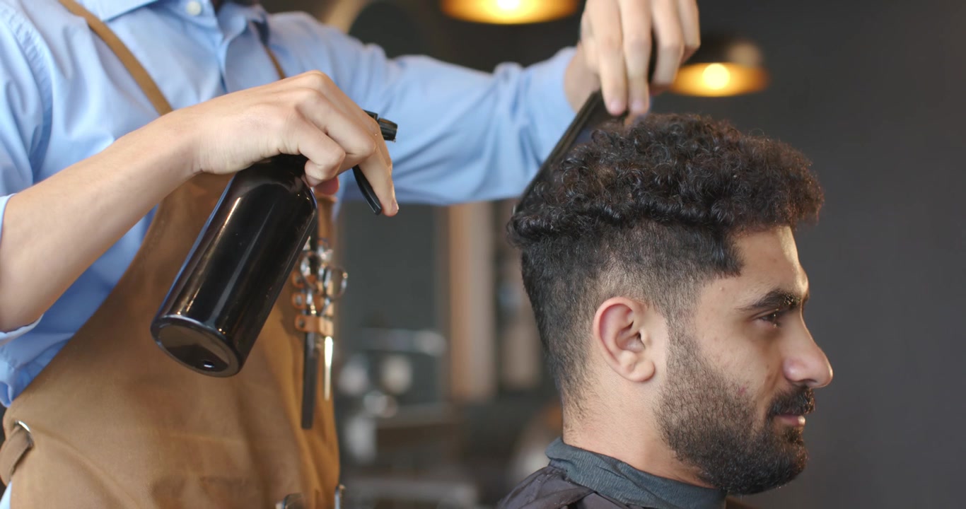 Afroamerikansk barber fugter kundens krøller med sprayflaske, reder og former en fade-frisure, med plads til tekst.