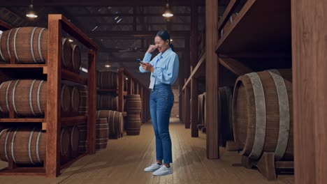 full body side view of an asian female professional worker standing with her phone in cellar of winery, she raises her fist up with screaming goal