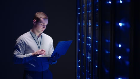 IT technician in data center digital server room controlling work of rack server cabinets with a tablet. Professional server engineer at work. Man technicians working in high tech server rack room