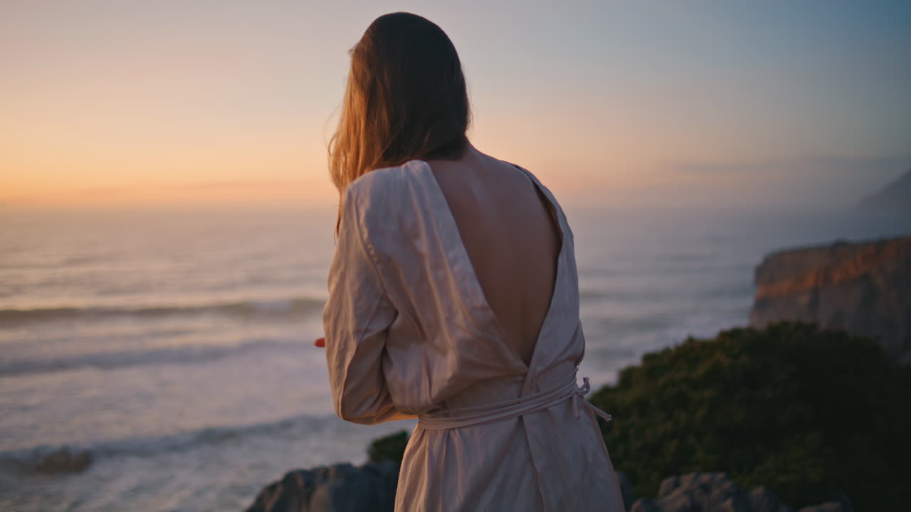 유연한 댄서가 저녁 해변에서 춤을 추며 손을 움직인다.