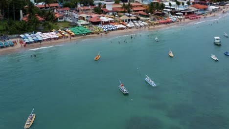 Aumento-De-La-Inclinación-Hacia-Abajo-Toma-Aérea-De-Drones-De-La-Playa-De-Porto-De-Galinhas-O-Puerto-De-Pollo-Con-Veleros-Anclados-Y-Cientos-De-Turistas-Nadando-En-El-Agua-Cristalina-Del-Océano-En-Pernambuco,-Brasil