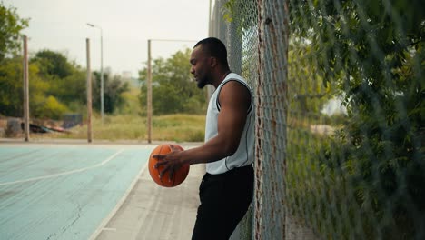 a young black man in a white t-shirt holds a basketball in his hands and waits for his entry to the basketball court to play. substitutes in teams of sports games