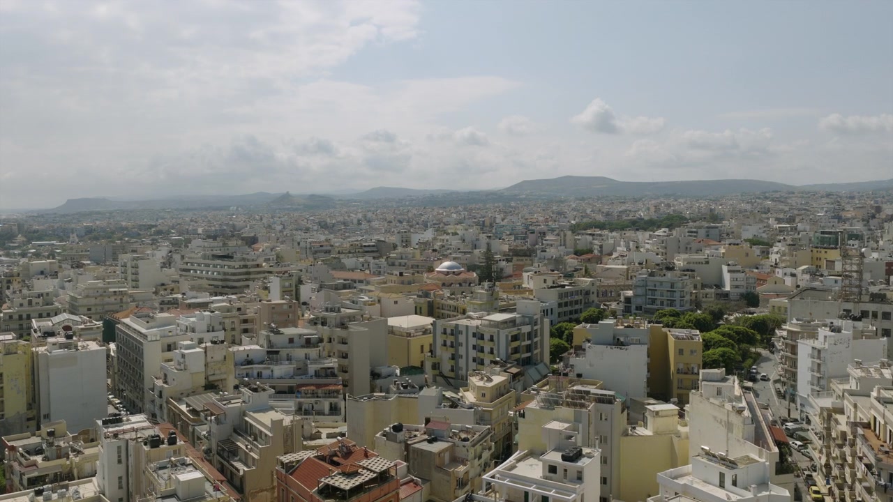 Panorama aereo di Heraklion, Creta, con edifici imbiancati a calce e color crema distribuiti in tutta la città e montagne che sfumano nella distanza nebbiosa