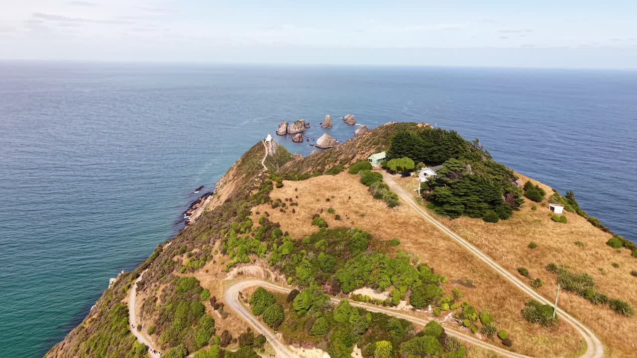 Forward drone shot over houses and path revealing cliffs, ocean and rocks at Nugget Point