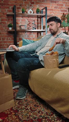 man relaxing at home with fried chicken and laptop