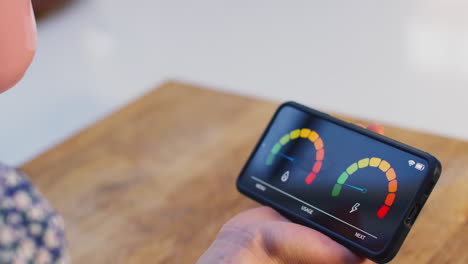 Close-up-of-woman-with-drink-holding-smart-energy-meter-measuring-electricity-and-gas-use-at-home---shot-in-slow-motion