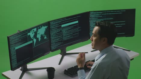 side view of asian man developer thinking about something while write code with multiple computer screens in green screen studio