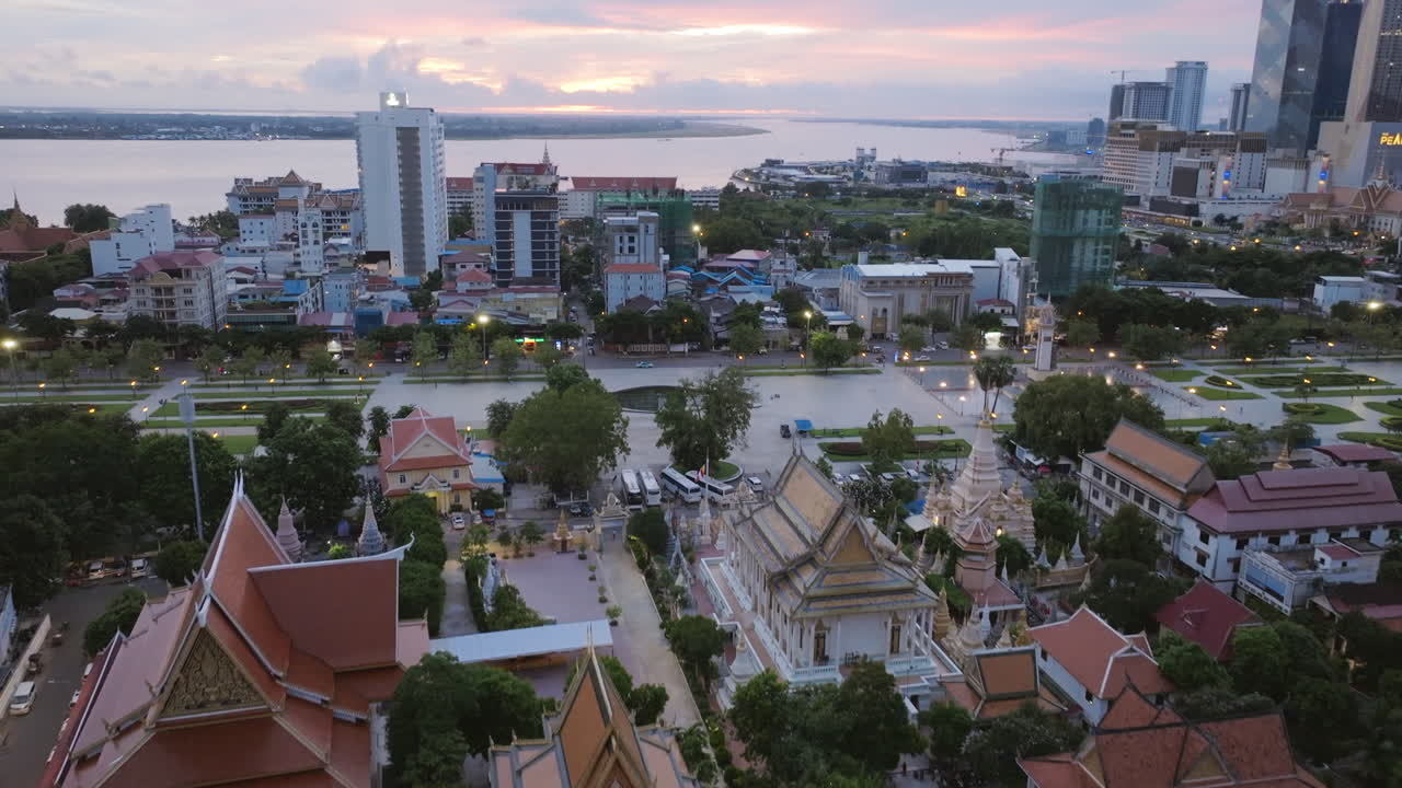 Aerial video of temple rooftops in Phnom Penh at dusk, with intricate spires and glowing lights lining the grounds