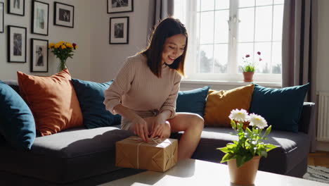 A young woman opens a gift package in her living room