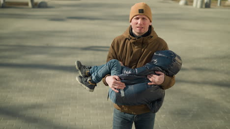 father carrying his sleeping child while walking, visibly stressed, the father is wearing a brown jacket and beanie, and the child is in black jacket, shadows are visible